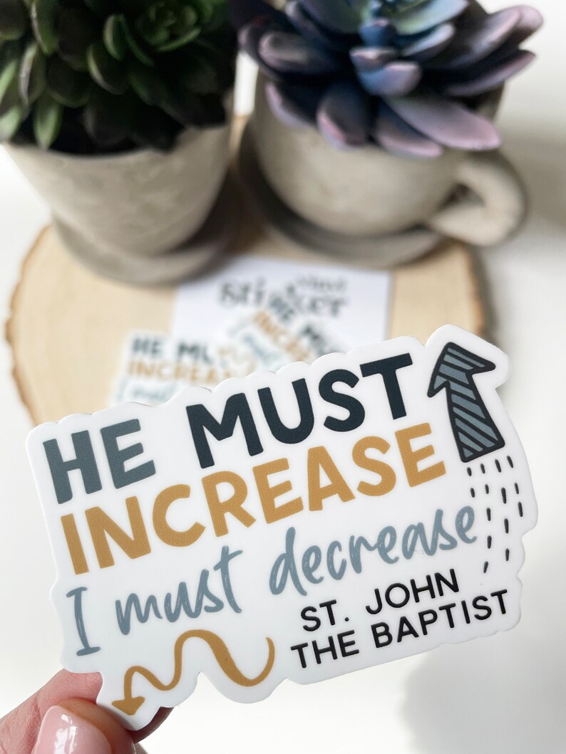 May include: White sticker with black, grey, and gold text that reads "He must increase, I must decrease!" with an arrow pointing up. Below the text is "St. John the Baptist".