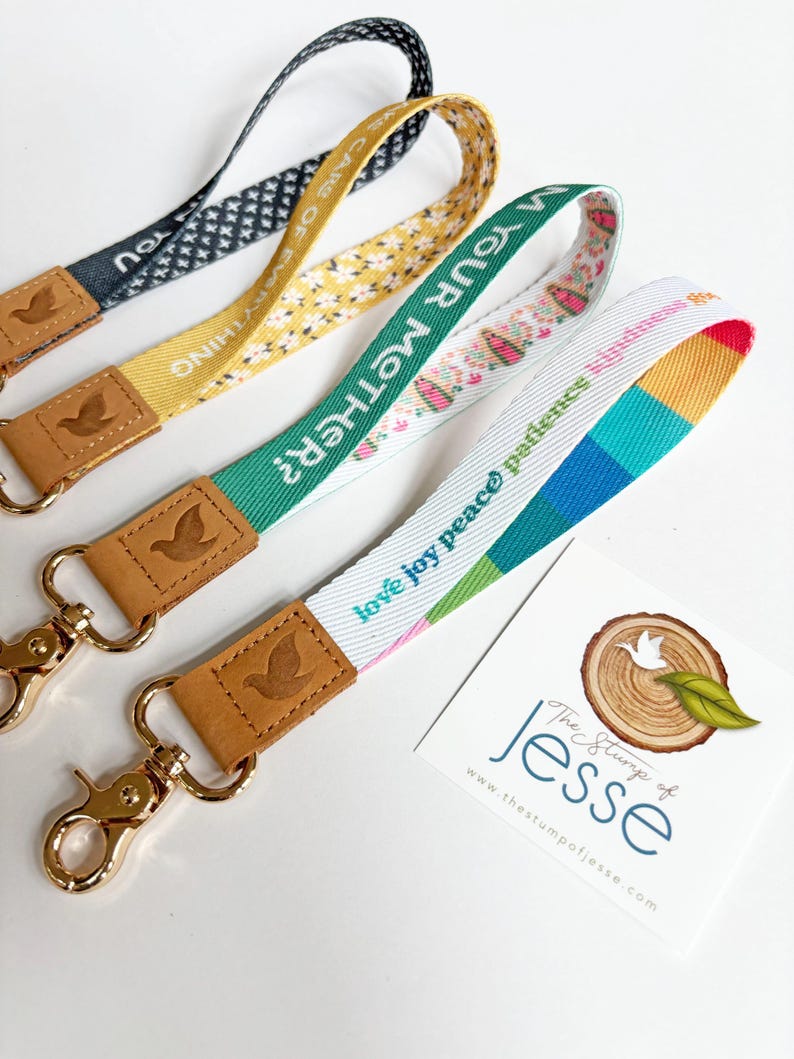 May include: Four fabric wristlet lanyards with gold-tone metal lobster clasps and tan leather tabs embossed with a bird icon. The straps feature various patterns and text including "take care of everything," "am your mother?" and "love joy peace."