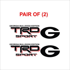 May include: A pair of Georgia Bulldogs Edition TRD Sport decals. Each decal has the TRD Sport logo in black and red, and a large black "G" logo. The text "PAIR OF (2)" is in red.