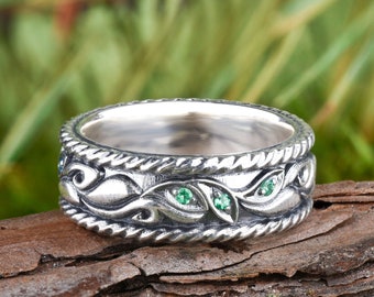 May include: A silver ring with a twisted band and a design of leaves with green gemstones.