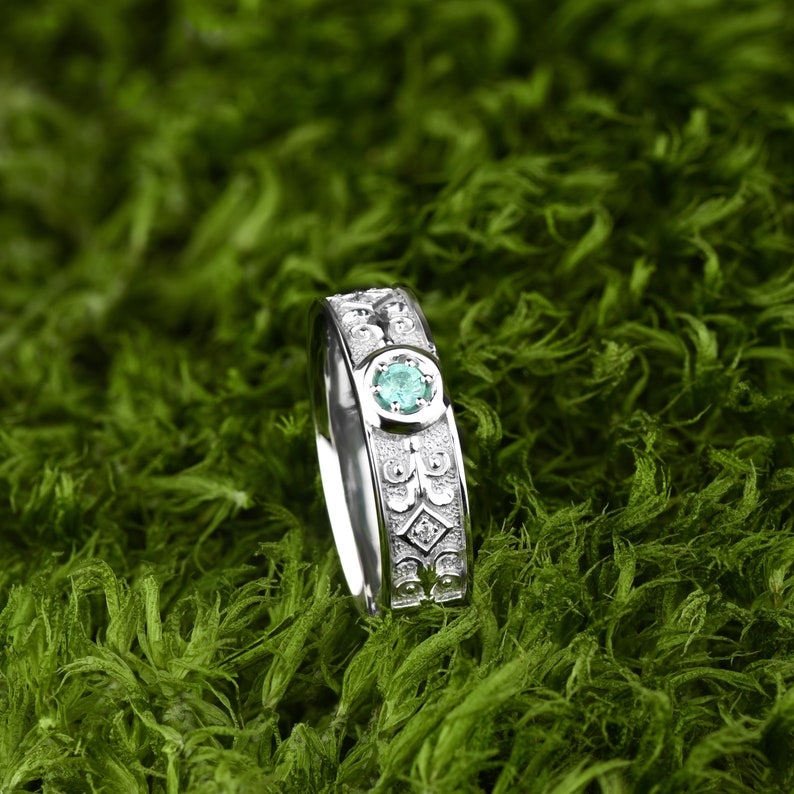 May include: A silver ring featuring an intricate design and a green gemstone at its centre.