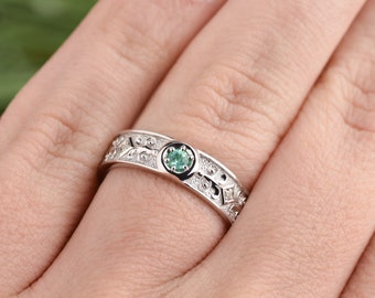 May include: A silver band ring with an intricate design and a small green gemstone in the center.