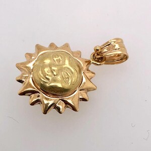 May include: A gold sun pendant with a face on it. The pendant is attached to a gold chain.
