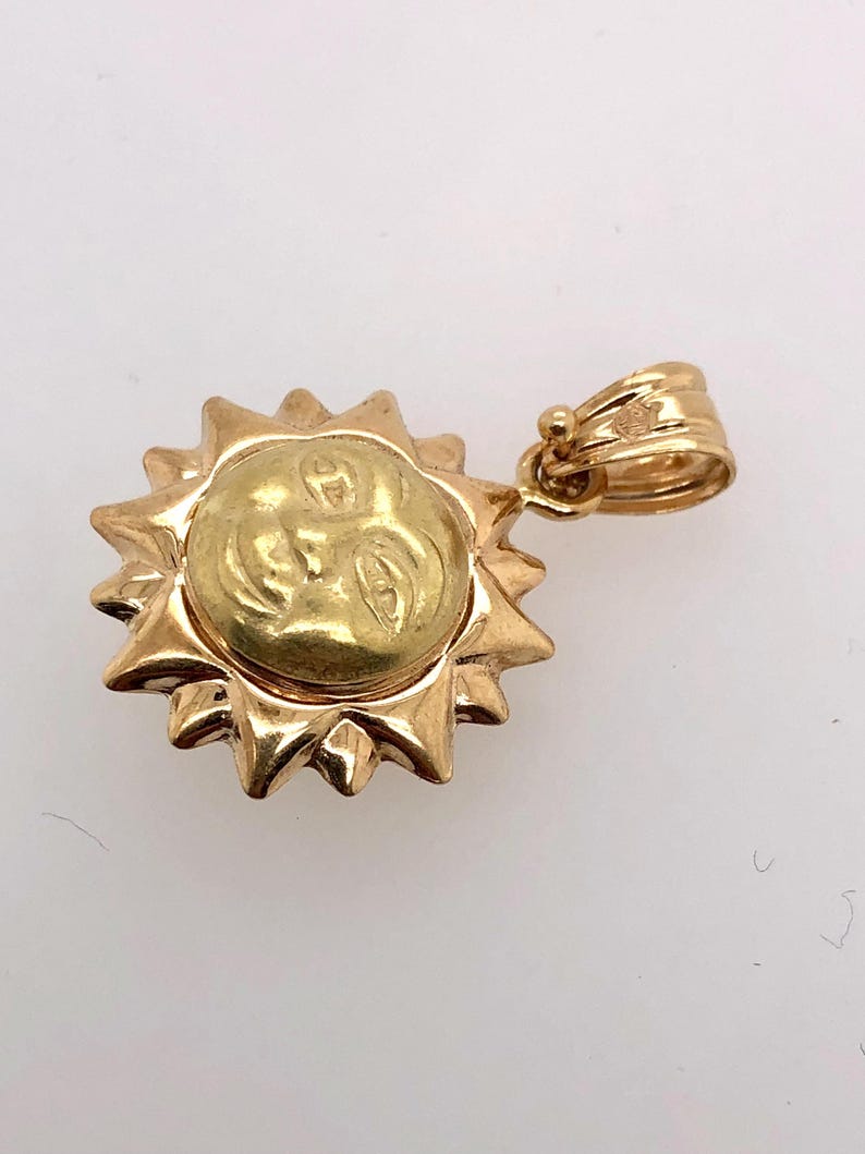May include: A gold sun pendant with a face on it. The pendant is attached to a gold chain.