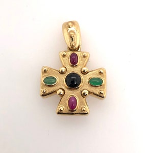 May include: A gold cross pendant with black, green, and red gemstones. The cross is detailed with small gold beads around the edges.