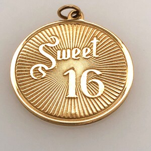 May include: Gold-toned round pendant with a sunburst design and the words "Sweet 16" in white lettering.