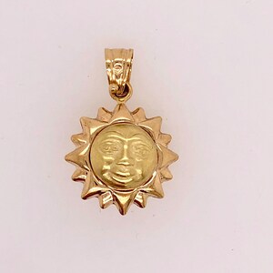 May include: A gold sun pendant with a face on it. The pendant is on a white background.