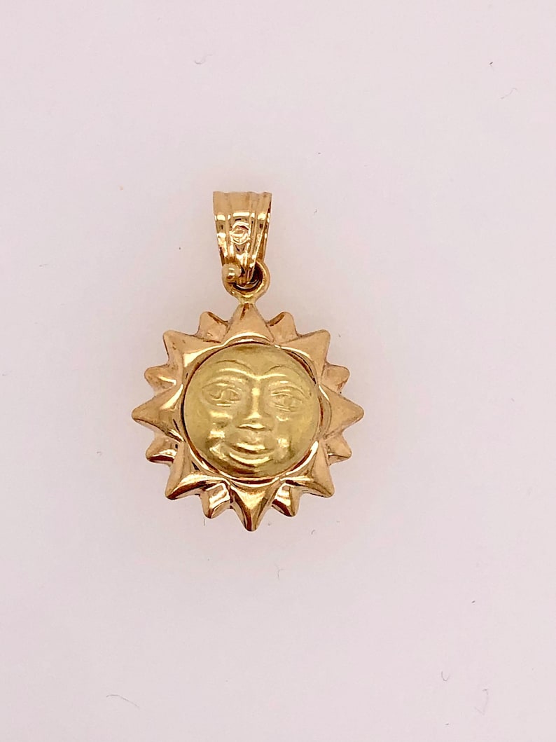 May include: A gold sun pendant with a face on it. The pendant is on a white background.