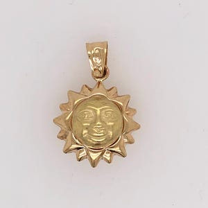 May include: A gold pendant charm in the shape of a sun with a face. The sun has a textured surface and a loop at the top for attaching to a chain.