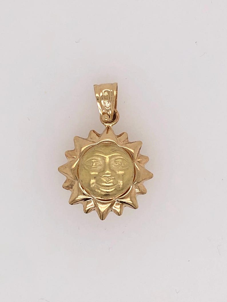 May include: A gold pendant charm in the shape of a sun with a face. The sun has a textured surface and a loop at the top for attaching to a chain.