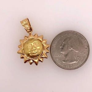 May include: A gold-toned sun pendant charm with a face on it. The pendant is about the size of a US quarter.