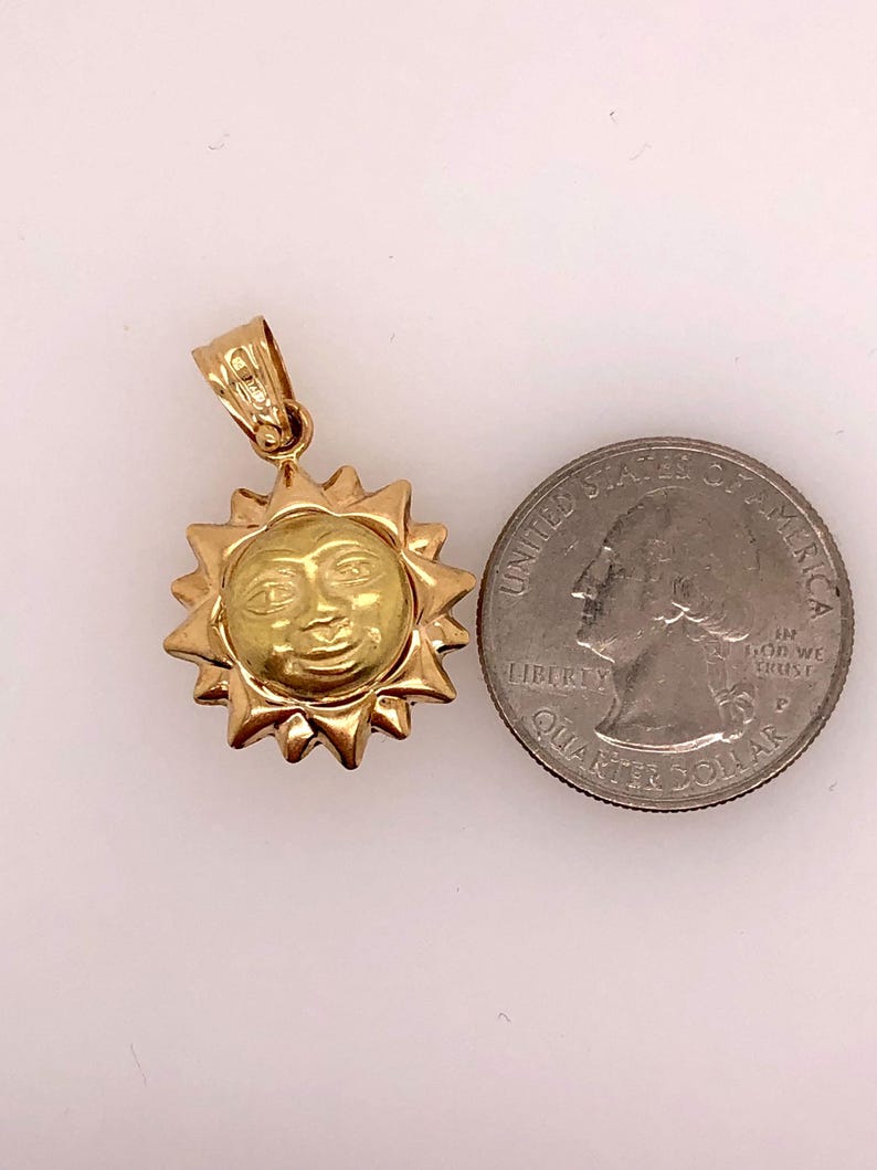 May include: A gold-toned sun pendant charm with a face on it. The pendant is about the size of a US quarter.