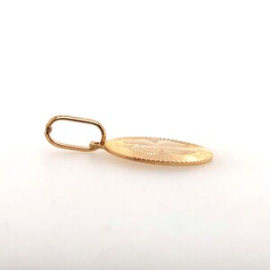 Pode incluir: Um pingente de ouro com um design oval texturizado. O pingente apresenta um padr&atilde;o detalhado e uma argola para uma corrente. O pingente &eacute; exibido em um fundo branco.