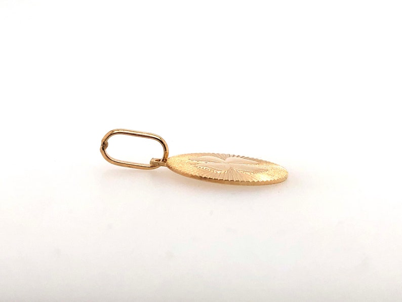 Pode incluir: Um pingente de ouro com um design oval texturizado. O pingente apresenta um padr&atilde;o detalhado e uma argola para uma corrente. O pingente &eacute; exibido em um fundo branco.