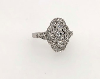 Puede incluir: Un anillo de plata con una gran piedra central de forma ovalada rodeada de diamantes más pequeños. El anillo tiene un diseño delicado e intrincado.