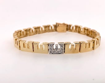 Pode incluir: Uma pulseira de ouro com um fecho em forma de letra 'U' cravejado de diamantes. A pulseira é feita de elos entrelaçados que se assemelham a pequenos edifícios.
