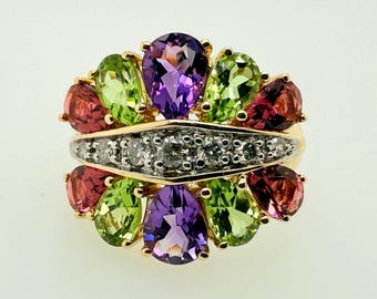 May include: A gold ring featuring a cluster of colorful gemstones. The ring showcases pear-shaped amethyst, peridot, and garnet stones, along with a band of small diamonds. The gemstones are arranged in a floral-like pattern.