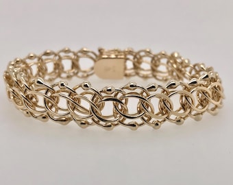 May include: A gold-colored bracelet with an intricate, open-link design. The bracelet features a series of interconnected oval and circular links, creating a delicate yet robust appearance. The clasp is also gold-toned, completing the cohesive look of the jewelry.