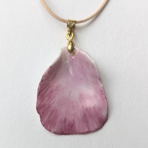 Puede incluir: Un delicado collar con un colgante de pétalo de rosa de porcelana rosa y blanco con una cadena dorada. El colgante tiene forma de pétalo de rosa y presenta un sutil degradado de rosa y blanco.