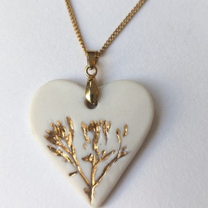 May include: A white ceramic heart pendant necklace with a gold chain and a gold leaf design.