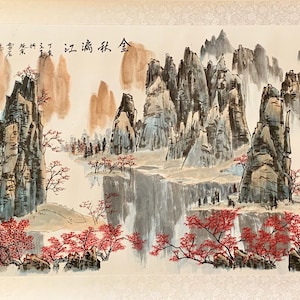 Puede incluir: Una pintura tradicional china de tinta y lavado que representa un paisaje montañoso con un río que lo atraviesa. Las montañas están representadas en tonos de gris y marrón, mientras que el río es de un azul claro. Hay árboles y flores en primer plano, pintados en tonos de rojo y verde. La pintura está firmada en caracteres chinos.