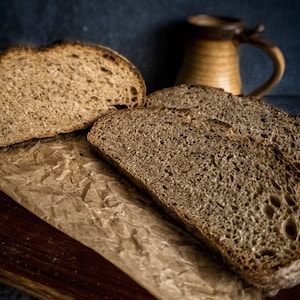 May include: Close-up of a loaf of freshly baked sourdough bread sliced on brown paper. The bread has a dark brown crust and a soft, airy crumb.