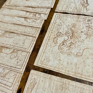 May include: A collection of vintage-style celestial maps, featuring constellations and star patterns. The maps are printed on aged paper with sepia-toned ink, creating an antique aesthetic. The arrangement suggests a focus on astronomy and historical cartography.