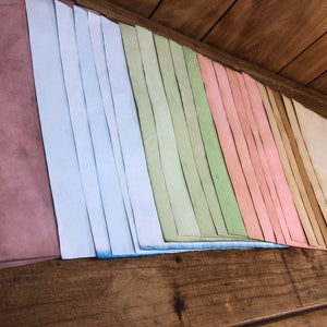 May include: A collection of colorful paper strips in shades of pink, blue, green, and brown. The strips are arranged in a rainbow pattern and are stacked on a wooden surface.
