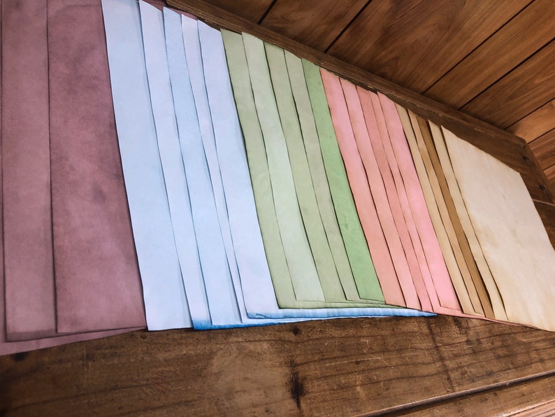 May include: A collection of colorful paper strips in shades of pink, blue, green, and brown. The strips are arranged in a rainbow pattern and are stacked on a wooden surface.