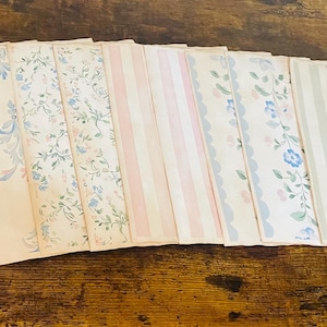 May include: A collection of vintage-style paper sheets with various patterns, including stripes and floral designs. The color palette features soft pastels like blue, pink, and green on a cream background. The papers are arranged in a fan shape, showcasing the variety of designs.