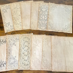 May include: A collection of vintage-style paper sheets with delicate lace patterns. The sheets are in various sizes and shapes, with intricate floral and geometric designs in white and cream colors. The edges of the paper have a slightly aged, antique look.