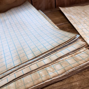 May include: A stack of vintage graph paper with blue lines. The paper is slightly yellowed and has a worn, aged look.
