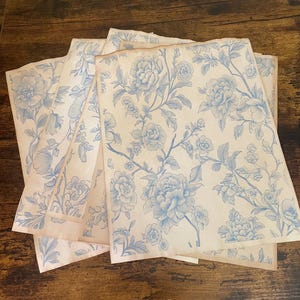 May include: A stack of vintage-style paper sheets with a light beige background and a blue floral pattern. The design features large peony-like flowers and delicate vines, creating a classic, romantic aesthetic.
