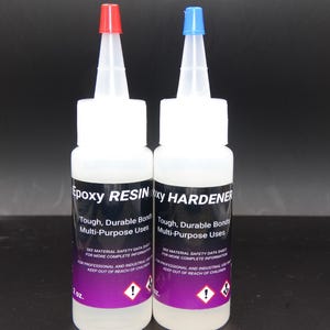 May include: Two white bottles of epoxy resin and hardener. The resin bottle has a red cap, and the hardener bottle has a blue cap. Each bottle has a black label with white text, including "Epoxy RESIN" and "HARDENER". The bottles are 2 oz.