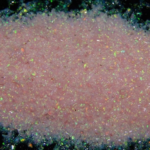 May include: A close-up of a pile of pink and iridescent glitter. The glitter is very fine and has a pearlescent sheen.