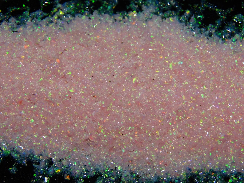 May include: A close-up of a pile of pink and iridescent glitter. The glitter is very fine and has a pearlescent sheen.