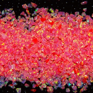 Puede incluir: Primer plano de un montón de vibrantes piedras preciosas de ópalo triturado. Los ópalos son principalmente de color rosa brillante con destellos de amarillo, verde y azul. Las piedras preciosas tienen forma irregular y son reflectantes.