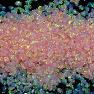 May include: Pink and iridescent opal chips, a type of crushed glass, with a rainbow effect. The chips are scattered on a black background.