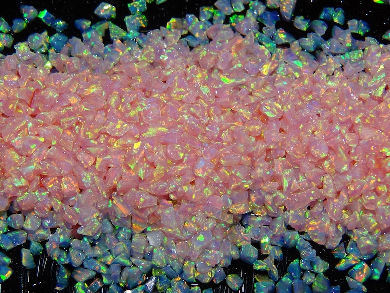 May include: Pink and iridescent opal chips, a type of crushed glass, with a rainbow effect. The chips are scattered on a black background.
