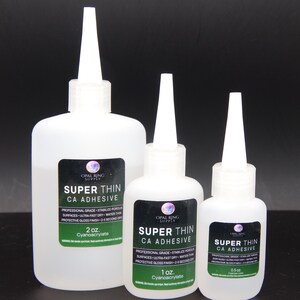 May include: Three white plastic bottles of Super Thin CA Adhesive, with white applicator tips. The bottles are labeled with black and green labels, and the sizes are 59 ml, 30 ml, and 15 ml.