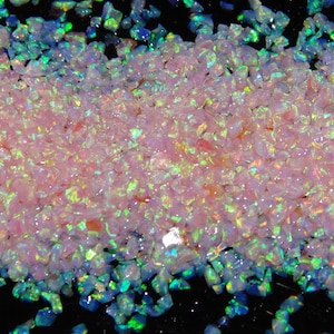 May include: A close-up of a pile of iridescent pink and green opal chips. The chips are small and irregular in shape, and they shimmer and sparkle in the light.