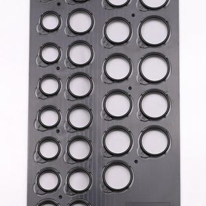 May include: A dark gray plastic gauge with multiple circular openings of varying sizes. Each opening has a white interior and a black border. The gauge is designed for measuring or sizing objects.