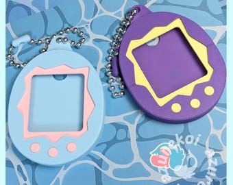 May include: Two oval-shaped silicone protective cases for digital pet devices. One case is light blue with a pink screen frame and three pink buttons. The other is purple with a yellow screen frame and three yellow buttons. Both have silver ball chains.