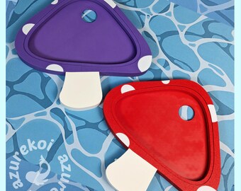 May include: Two mushroom-shaped trays, one purple and one red, each featuring a white stem and white spots on the cap. Each tray has a circular cutout on the cap surface. The text azurekoi is visible in the lower left corner of the image.