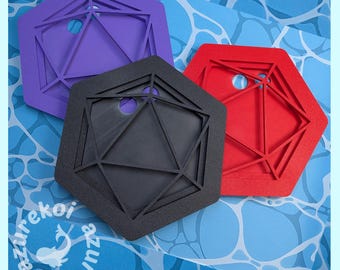 May include: Three hexagonal coasters in purple, black, and red, each featuring a raised geometric polyhedral die design with a circular cutout. The coasters are arranged in a cluster, showcasing a textured surface and sharp, angular lines.