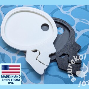 May include: Two skull-shaped decorative trays, one white and one dark gray, are displayed against a blue background with a water-like pattern. The white tray has a circular indentation. The image includes a "Made in and Ships from USA" sticker.