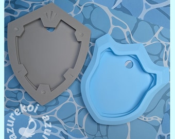 May include: A gray shield-shaped silicone mold and a light blue irregular-shaped silicone mold. Both molds feature recessed areas and circular indentations. The text azurekoi is printed in the bottom left corner of the image.