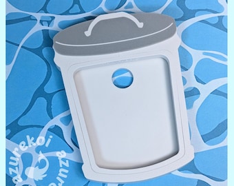 May include: A white trash can-shaped cookie cutter with a gray lid and a small circular cutout in the center. The cutter features a handle on the lid and is set against a blue background with a water-like pattern and the text azurekoi.
