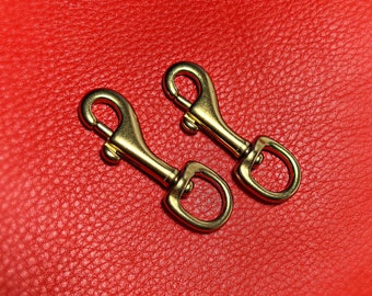 May include: Two gold-toned metal swivel clasps on a red textured surface.