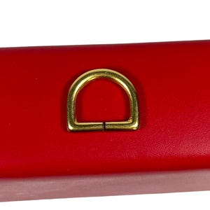 May include: A gold-colored metal D-ring on a red surface.